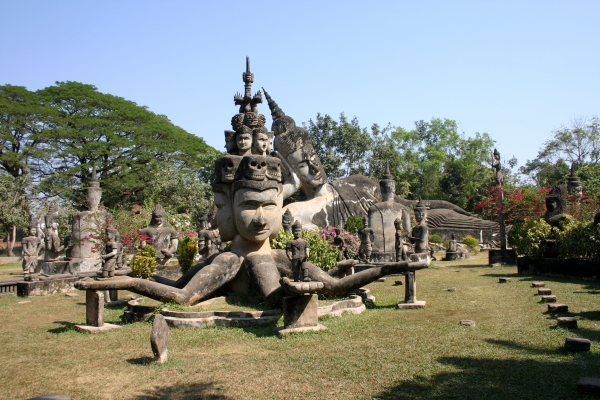 A statue with multiple faces and arms, in front of a Reclining Buddha