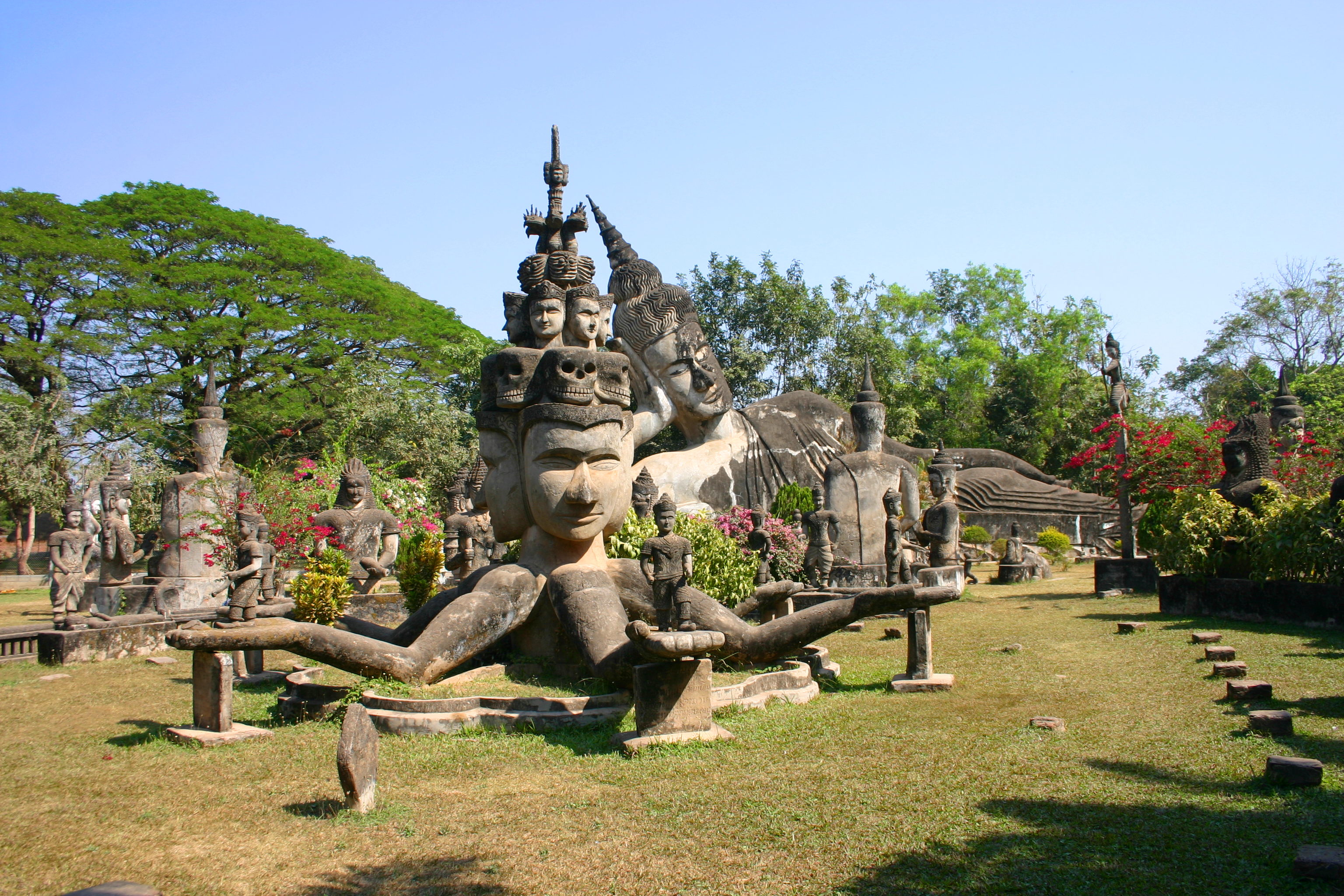 A statue with multiple faces and arms, in front of a Reclining Buddha